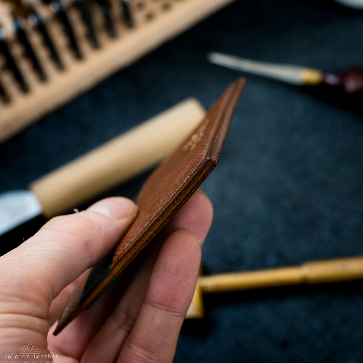 Hand holding a leather wallet with tools in the background