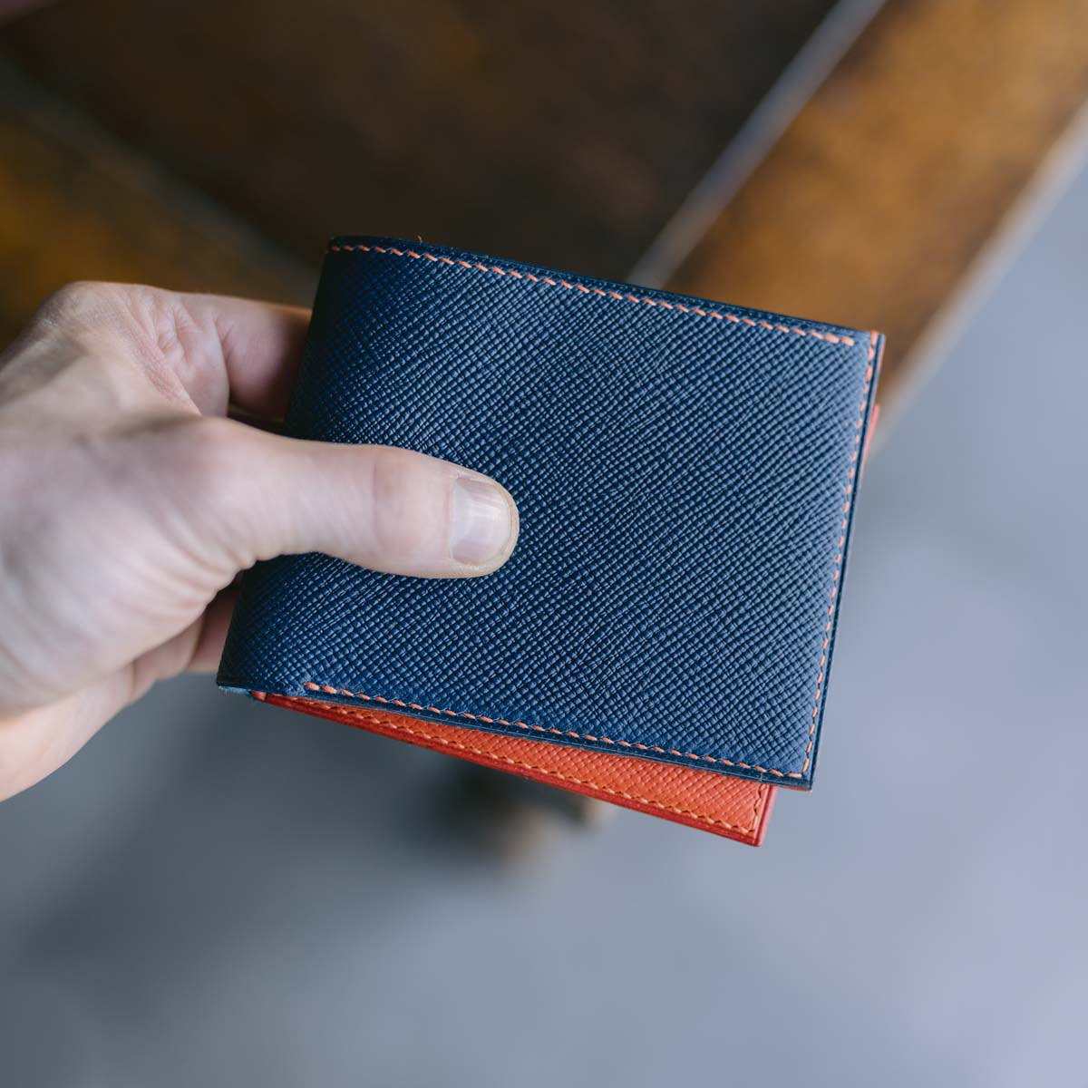 Hand holding a blue textured wallet with orange interior on a blurred background