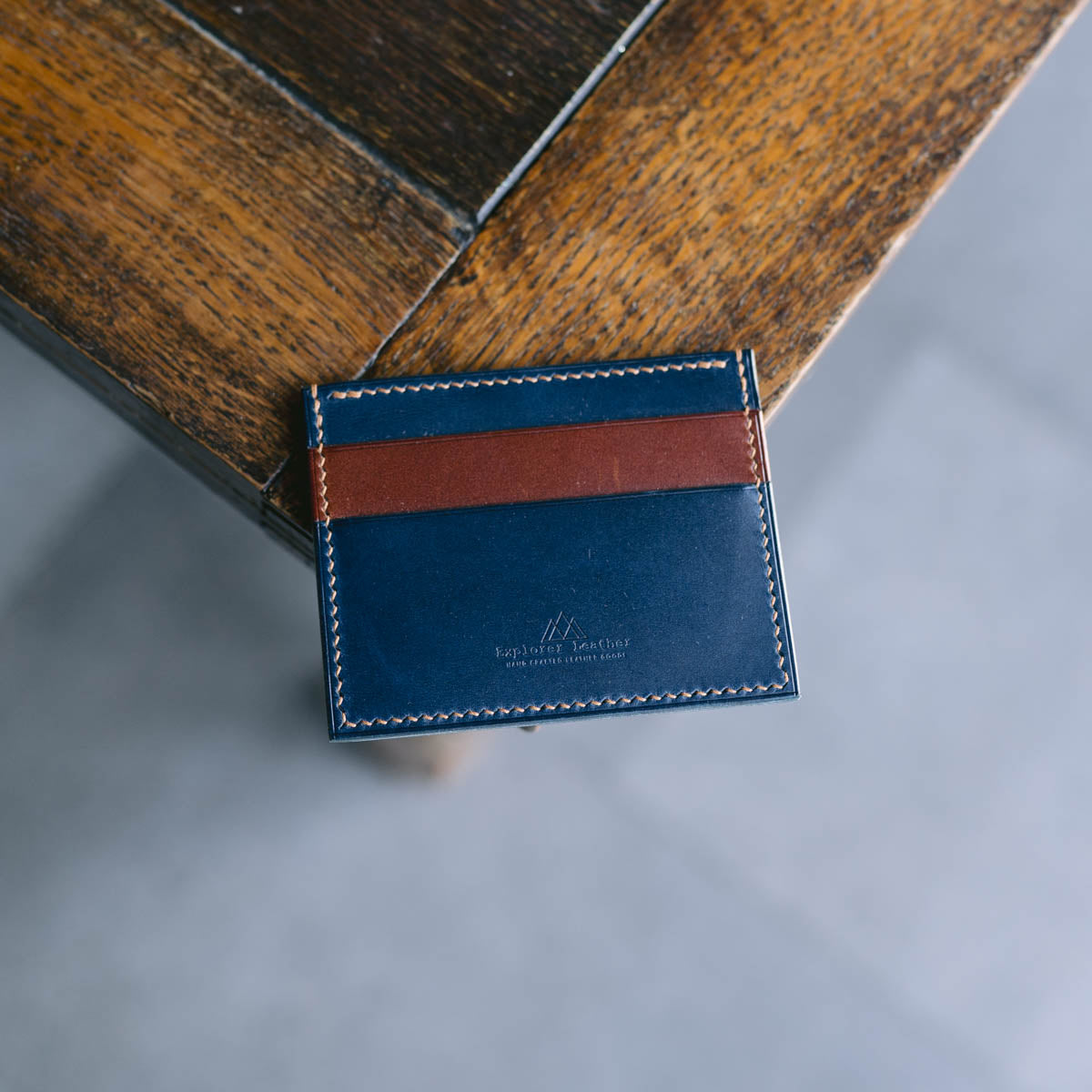 Blue leather cardholder with brown accent on a wooden surface