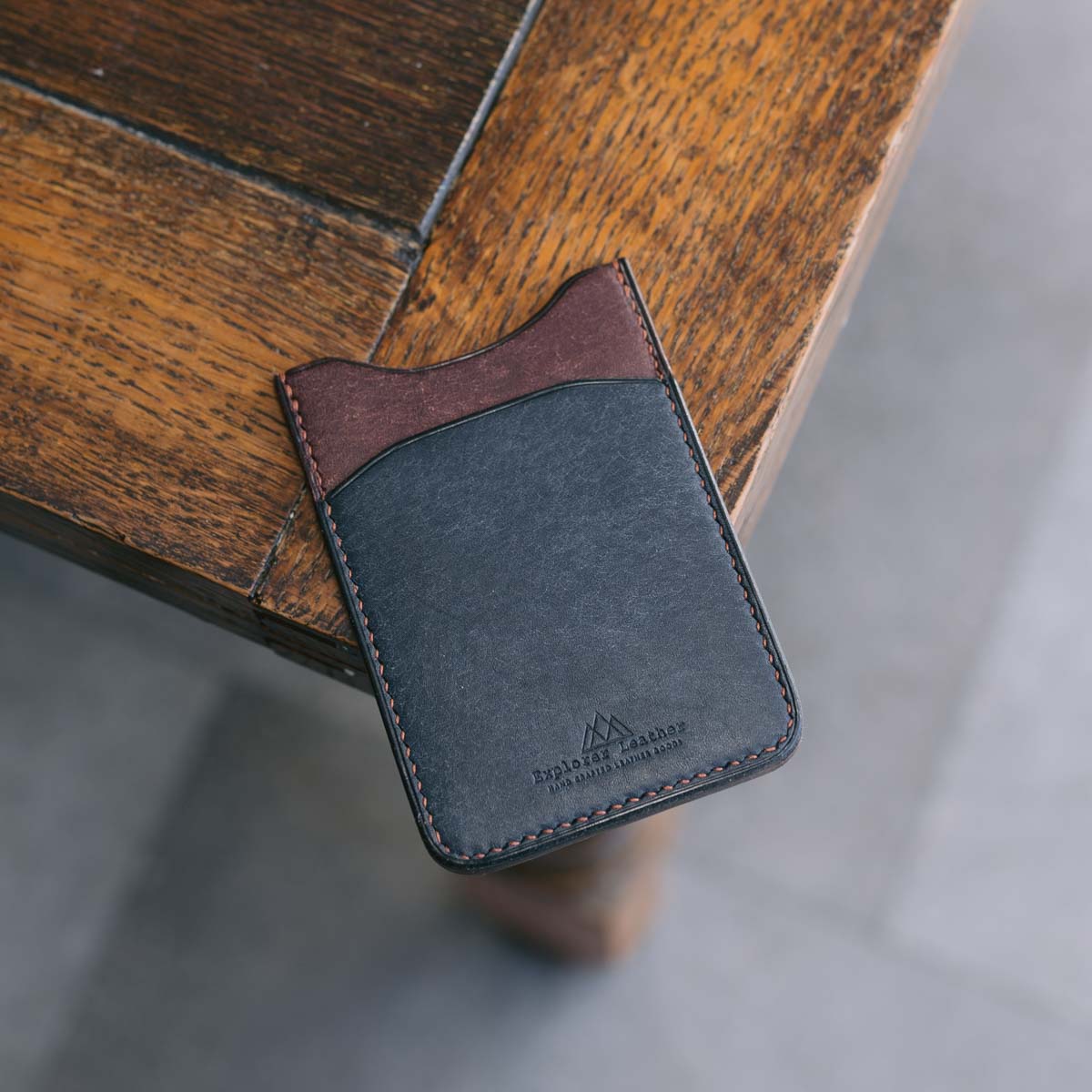 Hand holding a Blue and Brown leather cardholder on a wooden surface.