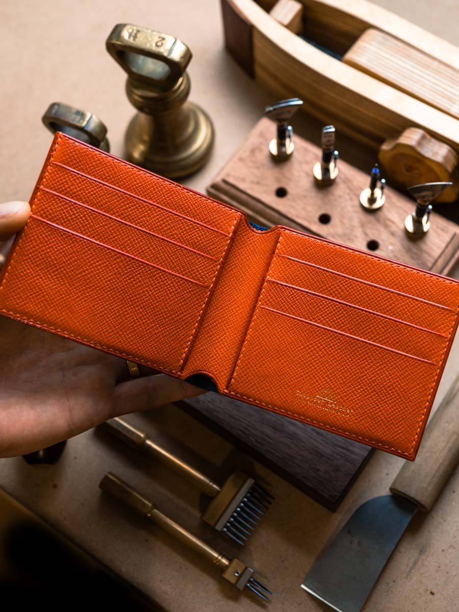 Open navy leather bifold wallet showing orange interior