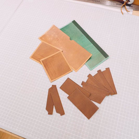 Cut leather panels and pocket pieces for a handmade bifold wallet laid out on a workbench