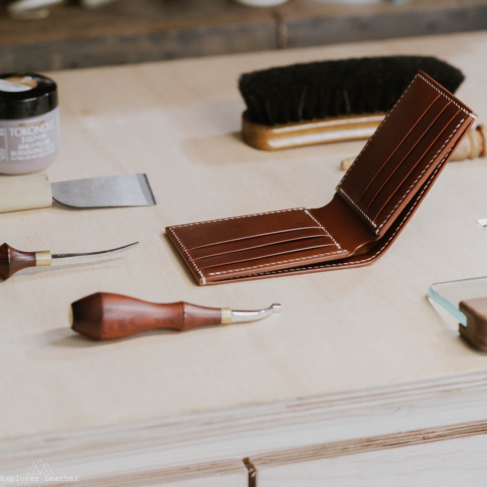 brown tan bi-fold leather wallet, white stitching, leather hand tools