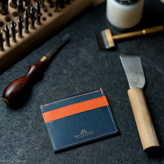 Blue and orange cardholder on a dark surface with leather tools