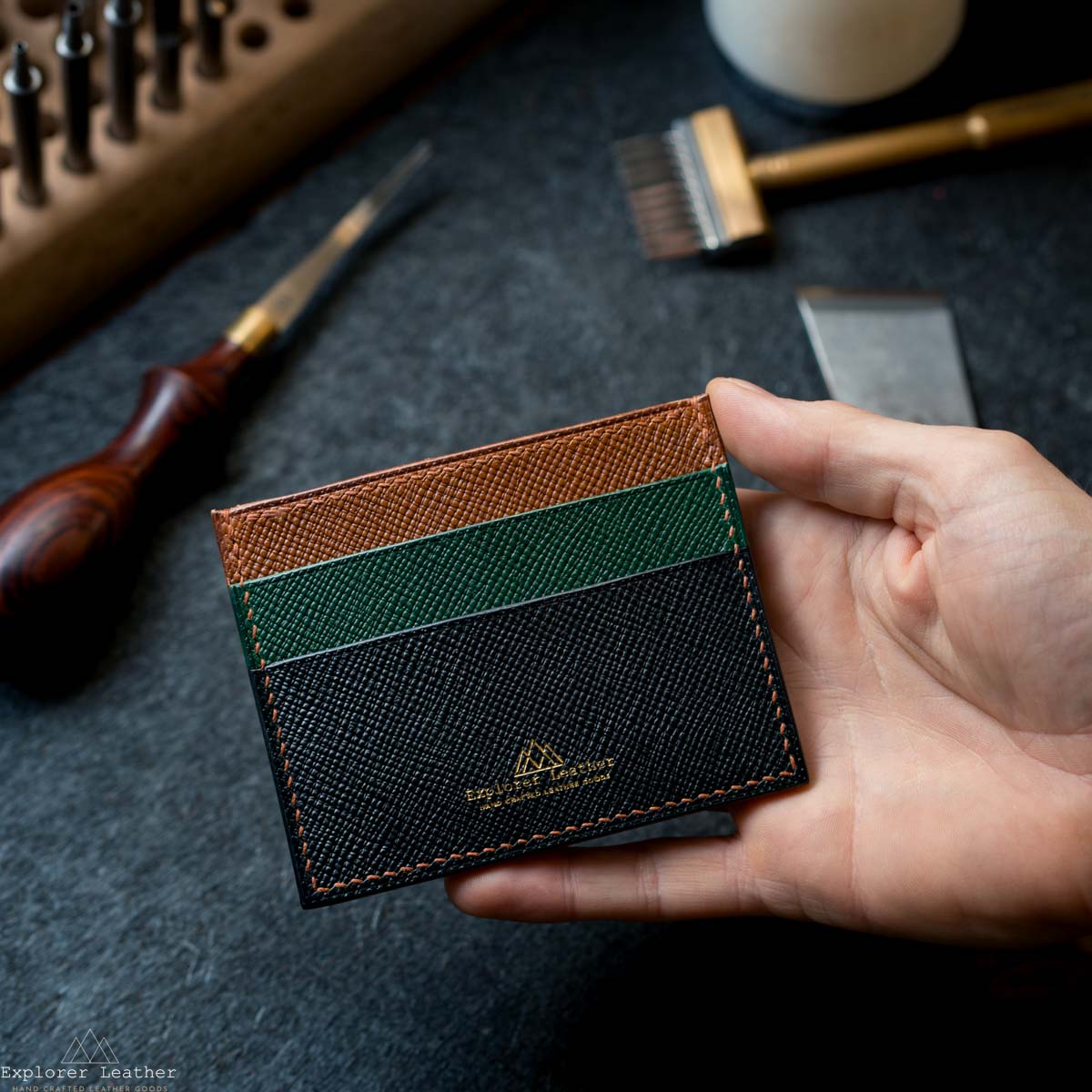 Hand holding a leather cardholder with a textured design on a dark surface.