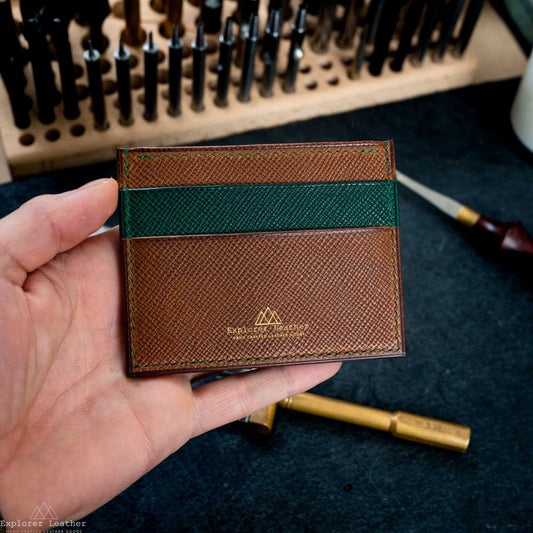 Brown leather cardholder with green pocket held by a hand, with tools in the background