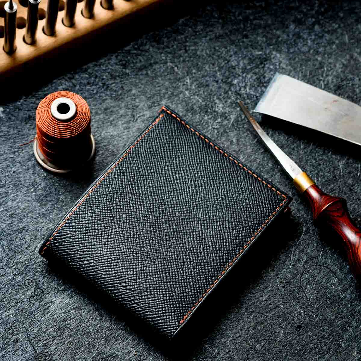 Black leather wallet with sewing tools on a dark surface. walpier buttero hatch leather