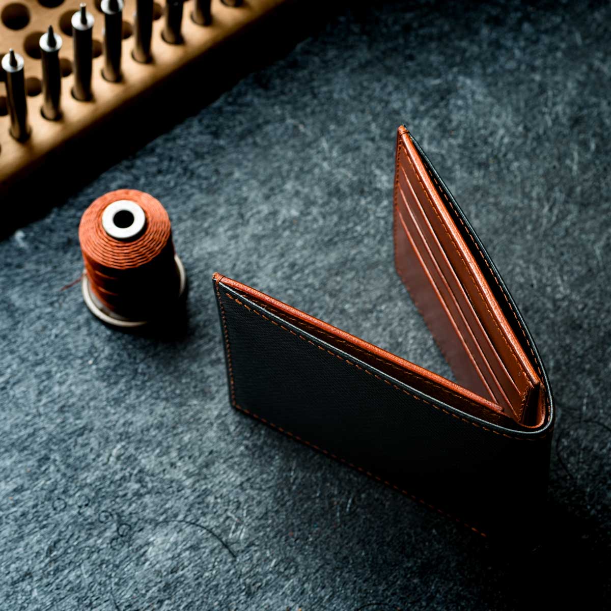 Brown leather wallet on a dark textured surface with sewing thread and needle in the background.