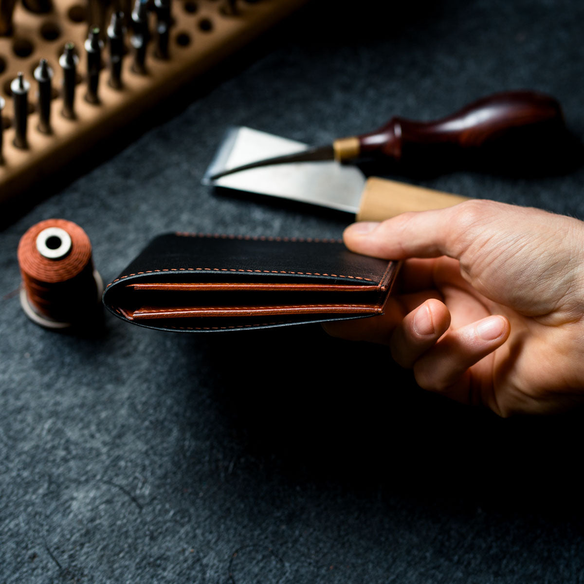 Hand holding a leather wallet with tools on a dark surface