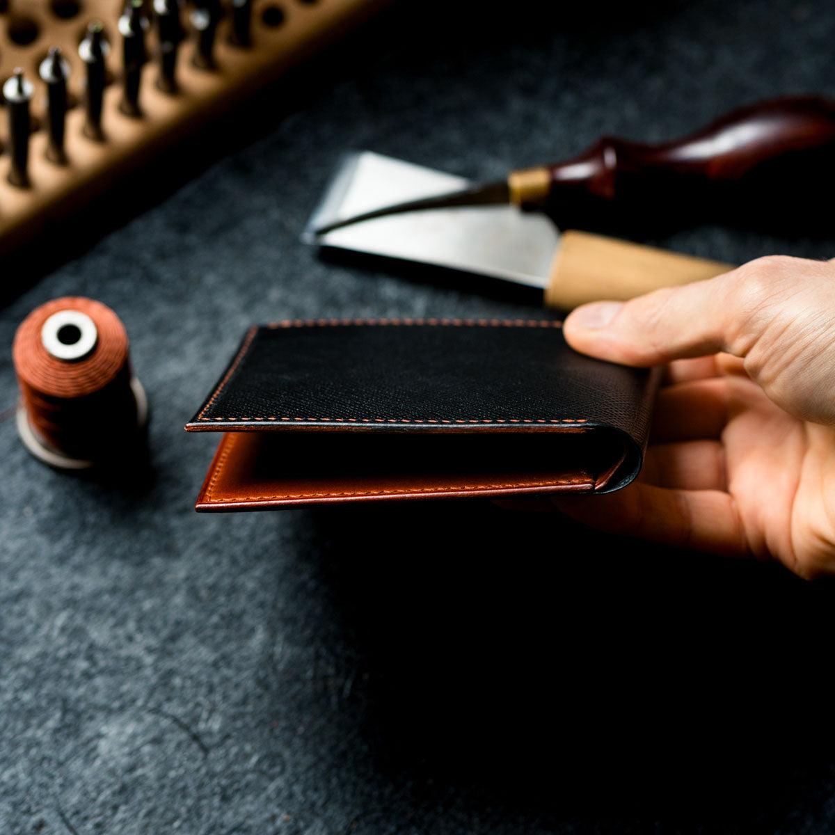 Hand holding a leather wallet with tools and materials on a dark surface