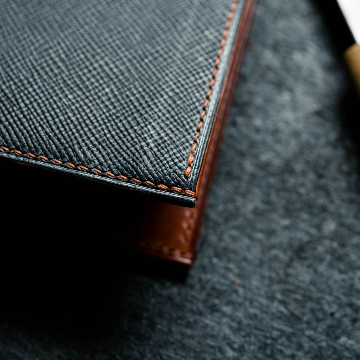 Close-up of a textured black leather wallet with brown stitching on a dark surface.