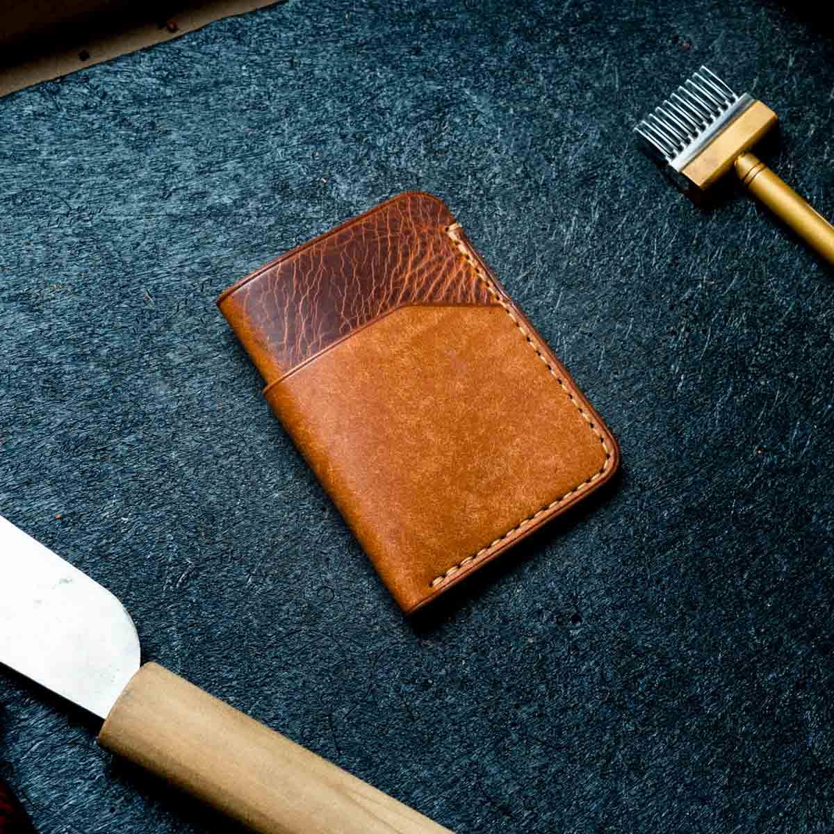 Brown leather wallet on a textured dark surface with grooming tools.