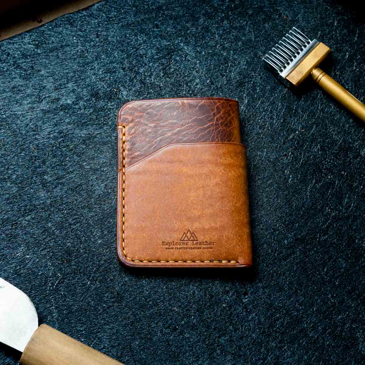 Brown leather wallet on a dark textured surface with a tool in the background