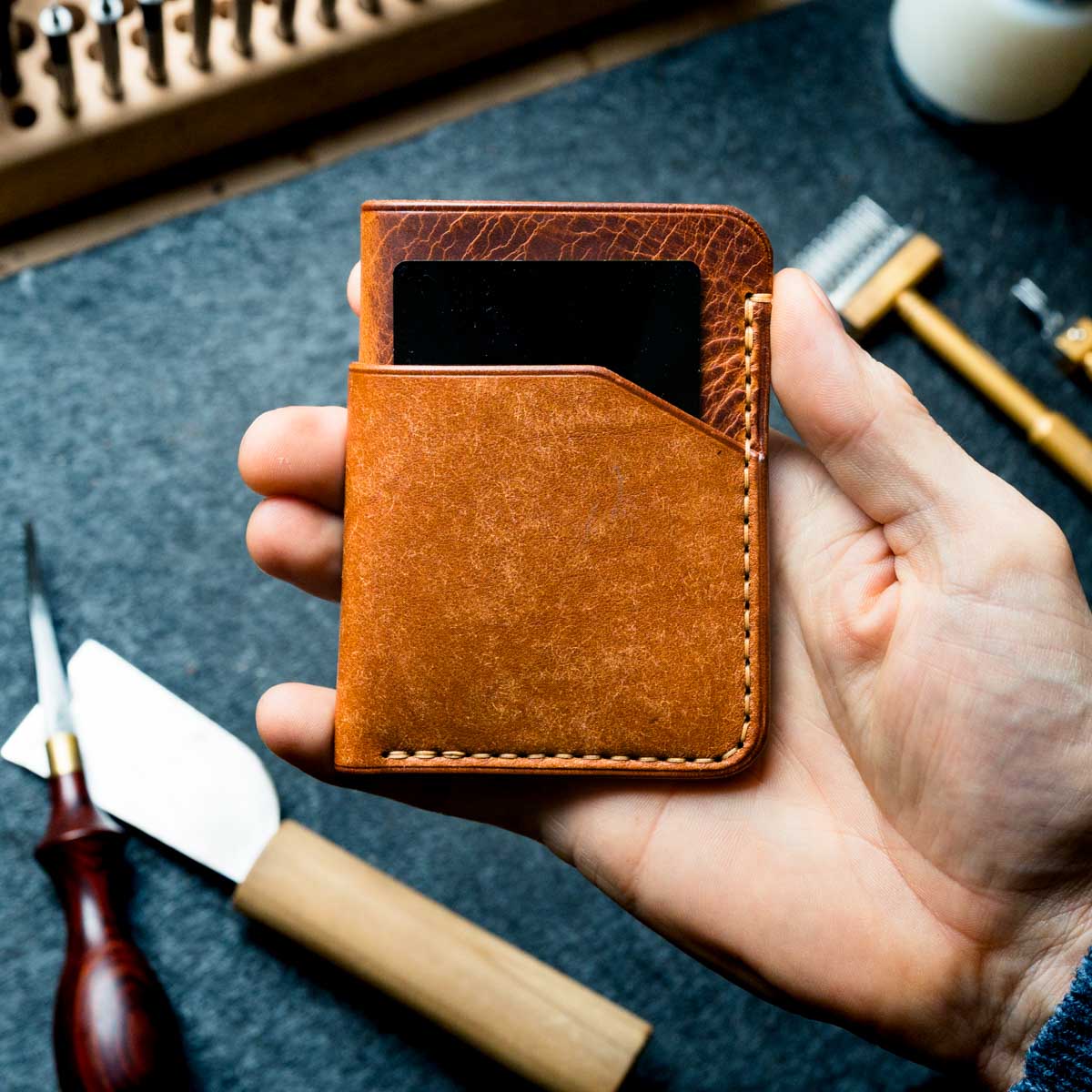 Hand holding a brown leather wallet with tools in the background