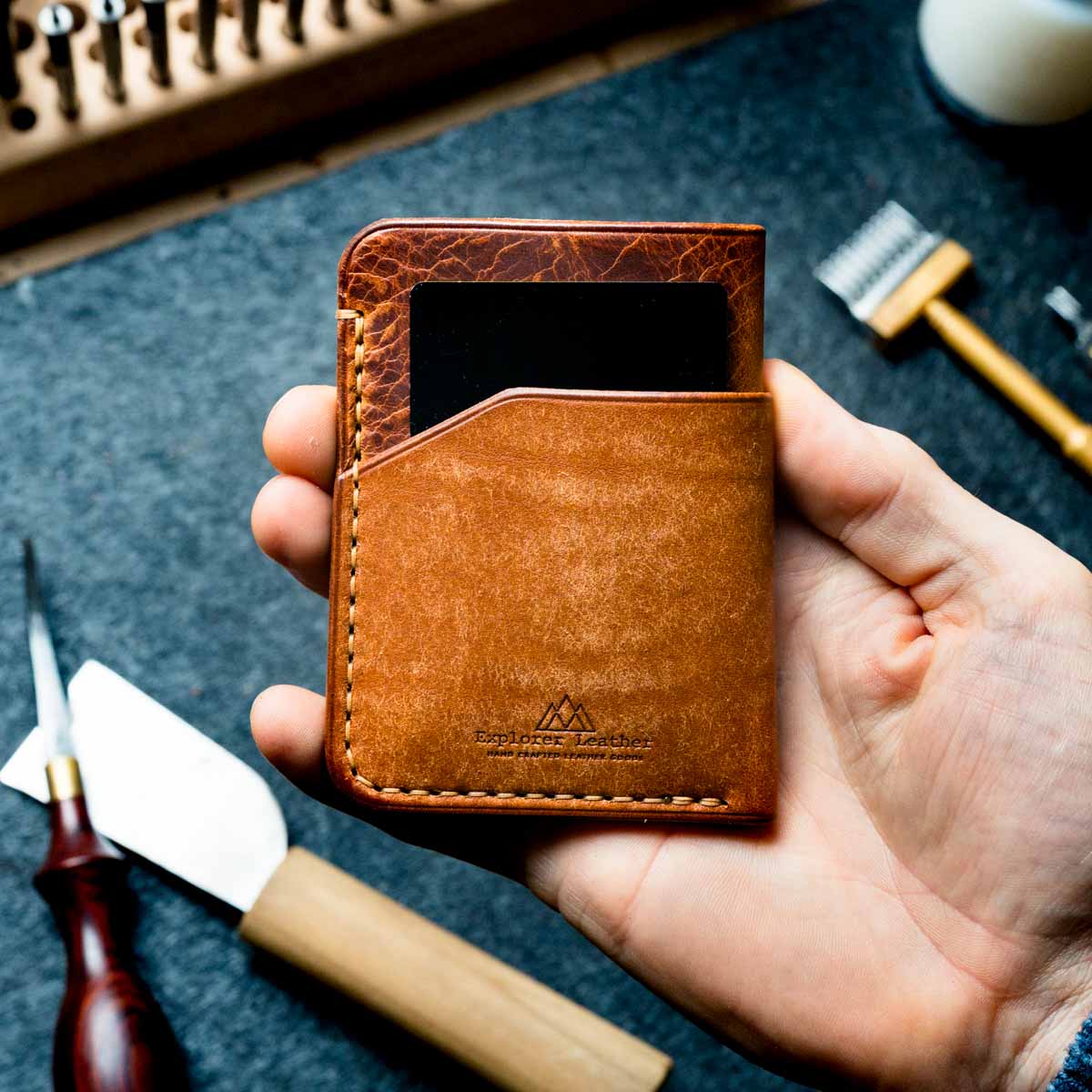 Brown leather wallet held in a hand with tools in the background