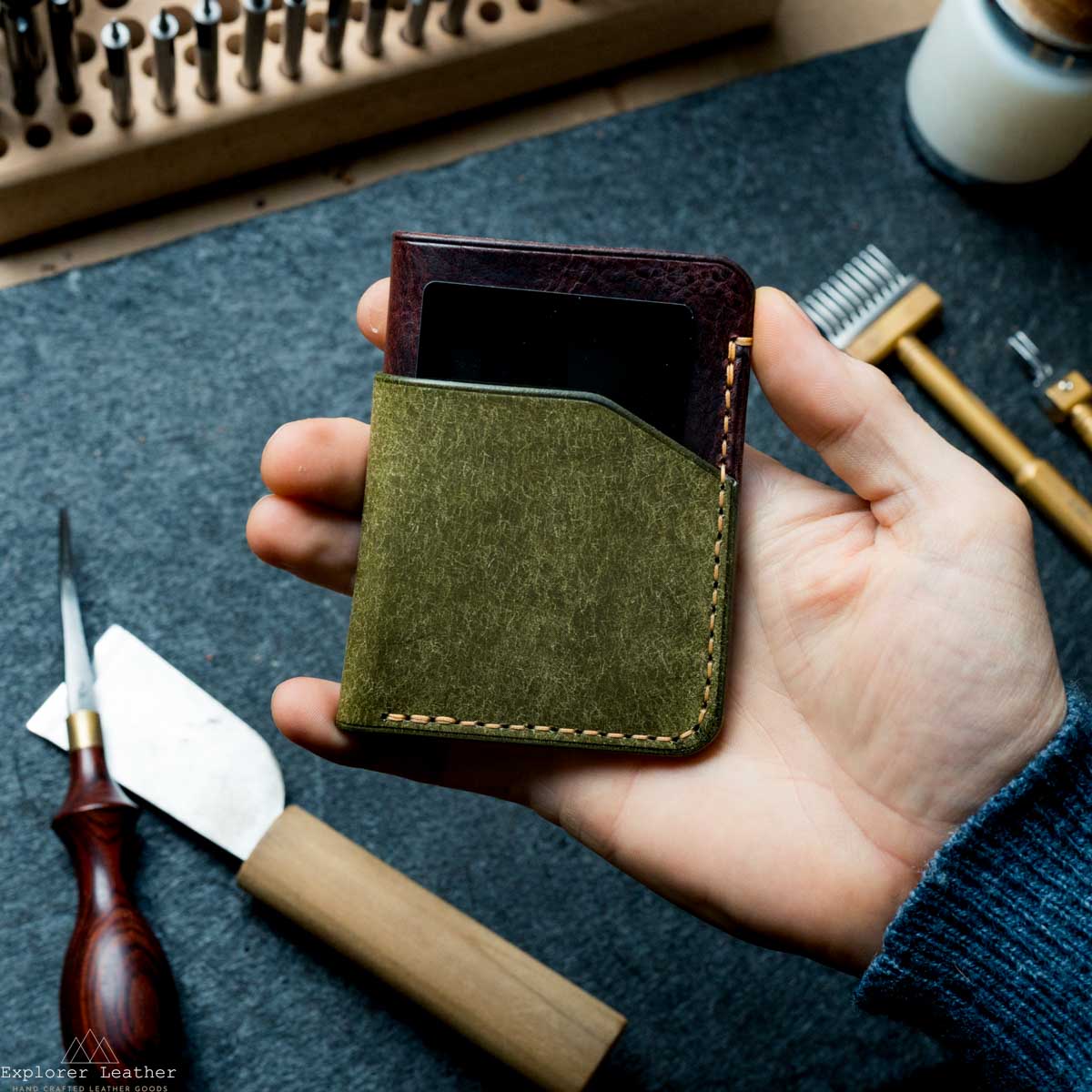 Hand holding a green leather wallet with tools in the background