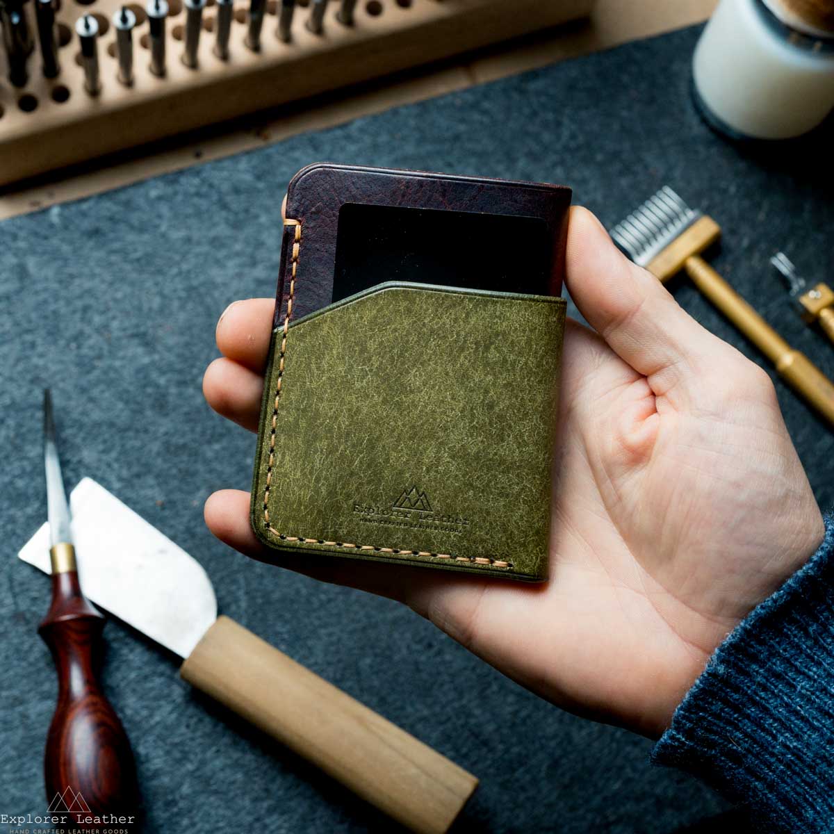 Hand holding a green leather wallet with tools in the background