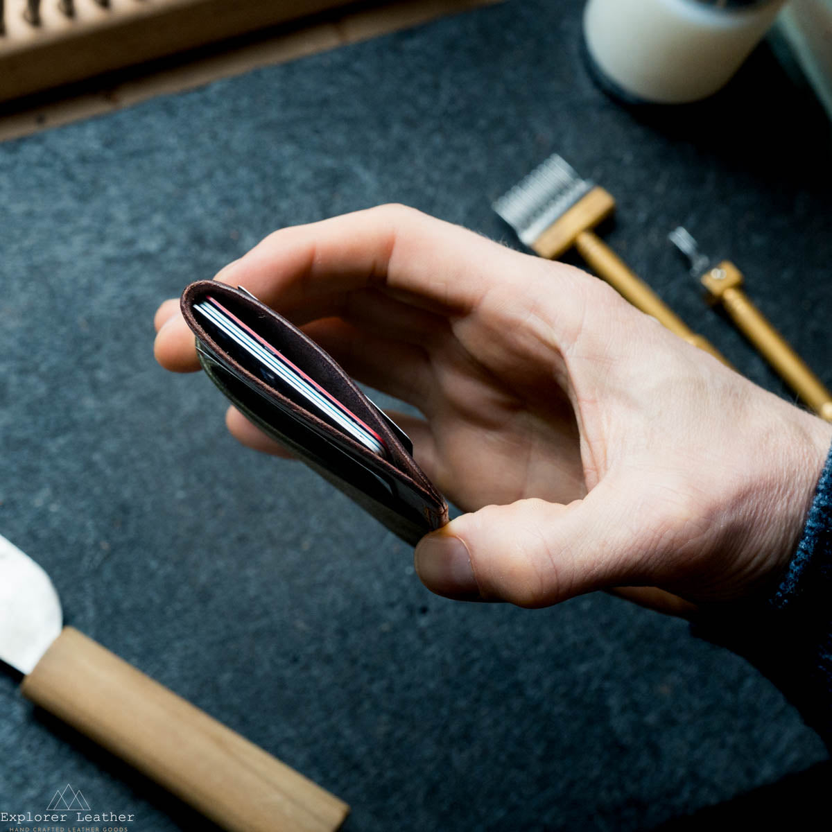 Hand holding a leather wallet with tools in the background