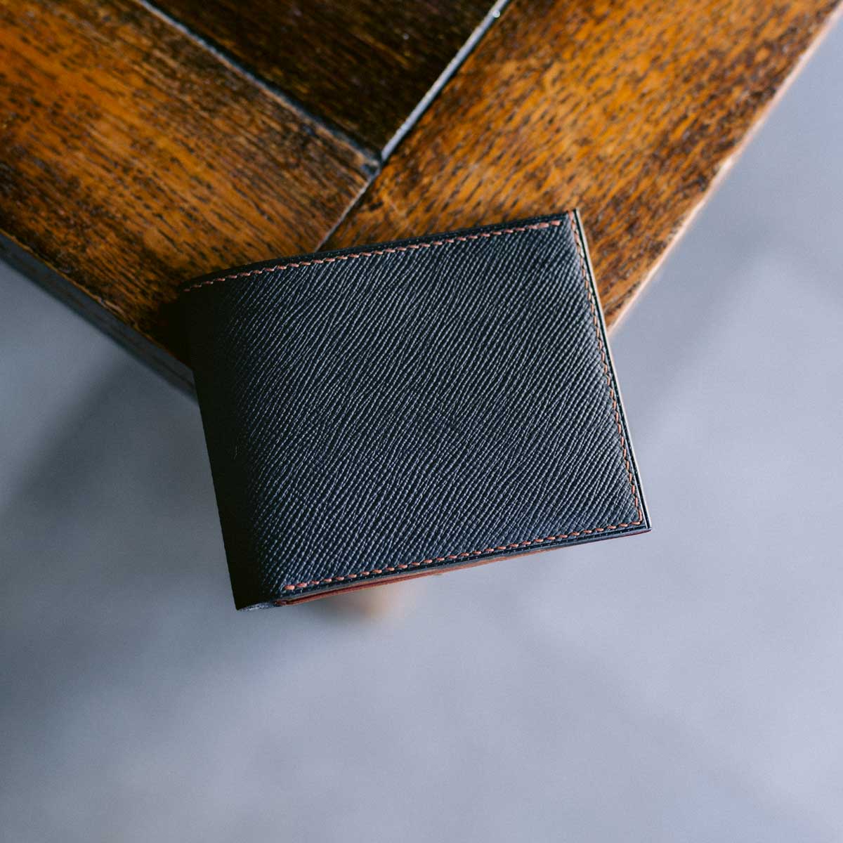 Black leather wallet with brown stitching on a wooden surface
