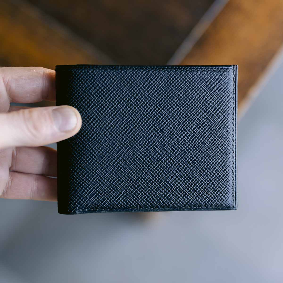Hand holding a black textured wallet against a neutral background