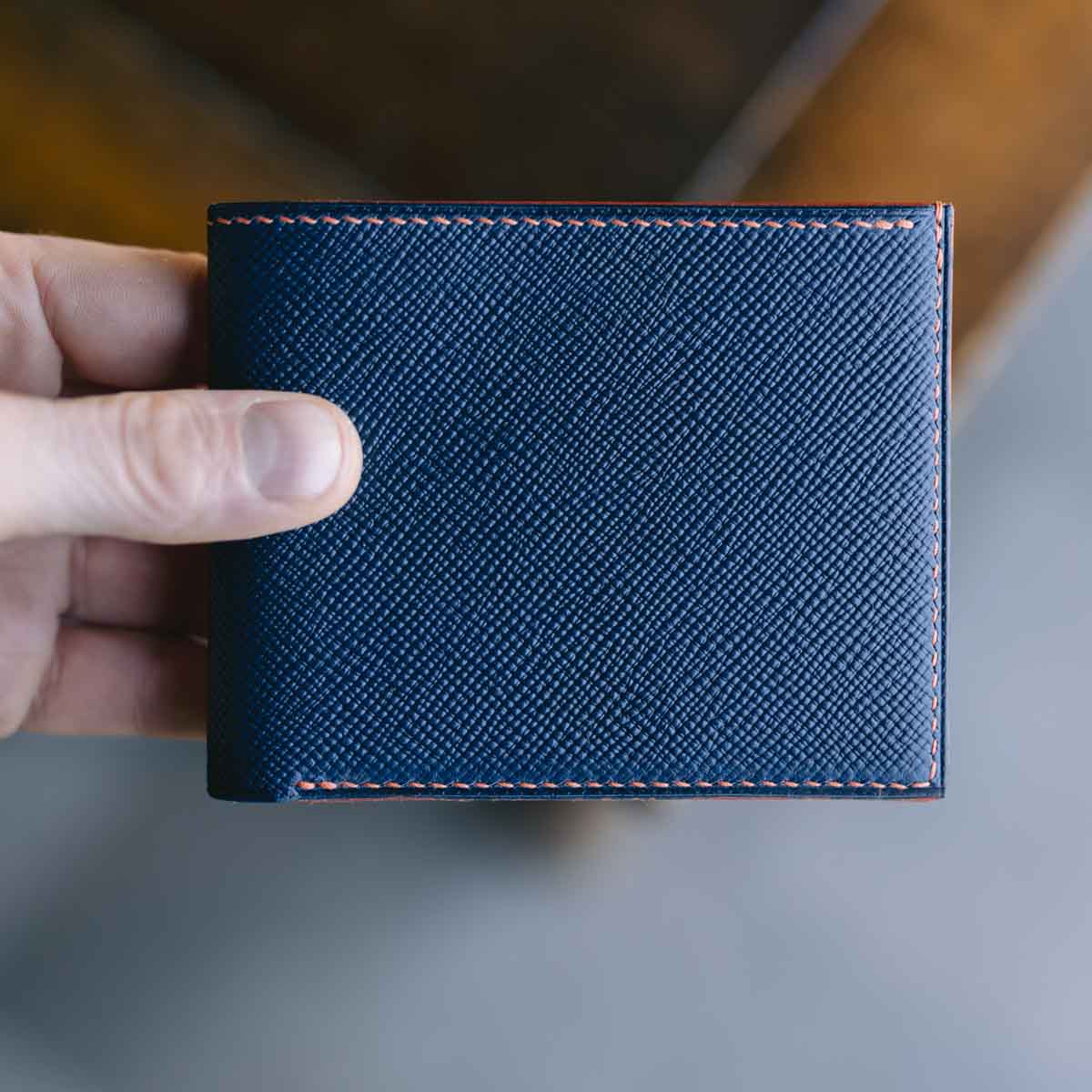 Hand holding a blue and orange textured wallet against a blurred background