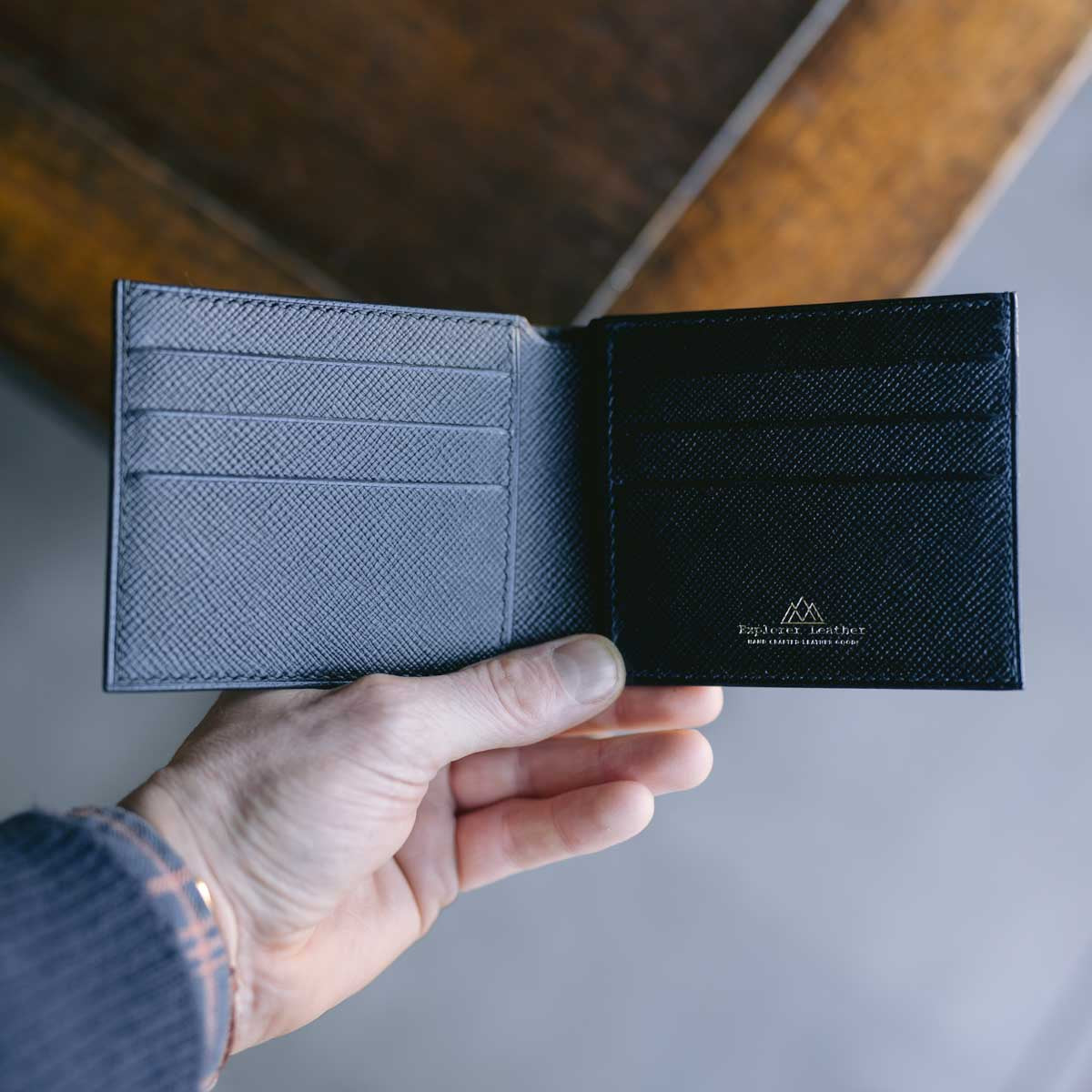 Hand holding a black leather wallet with a visible brand logo on a neutral background