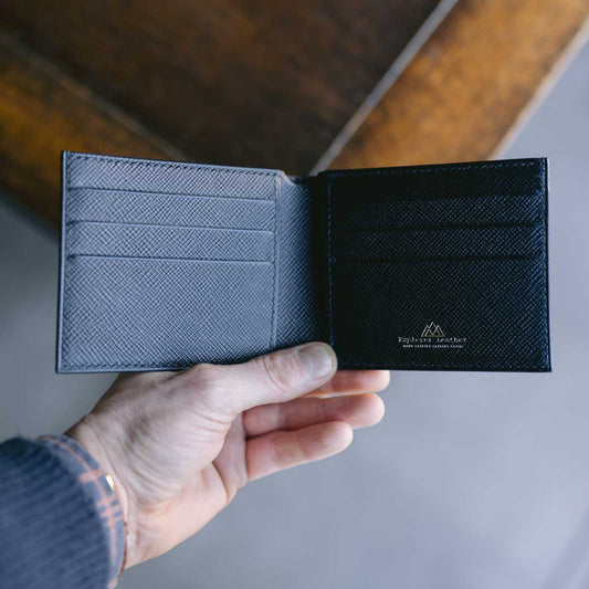 Hand holding a black leather wallet with a visible brand logo on a neutral background