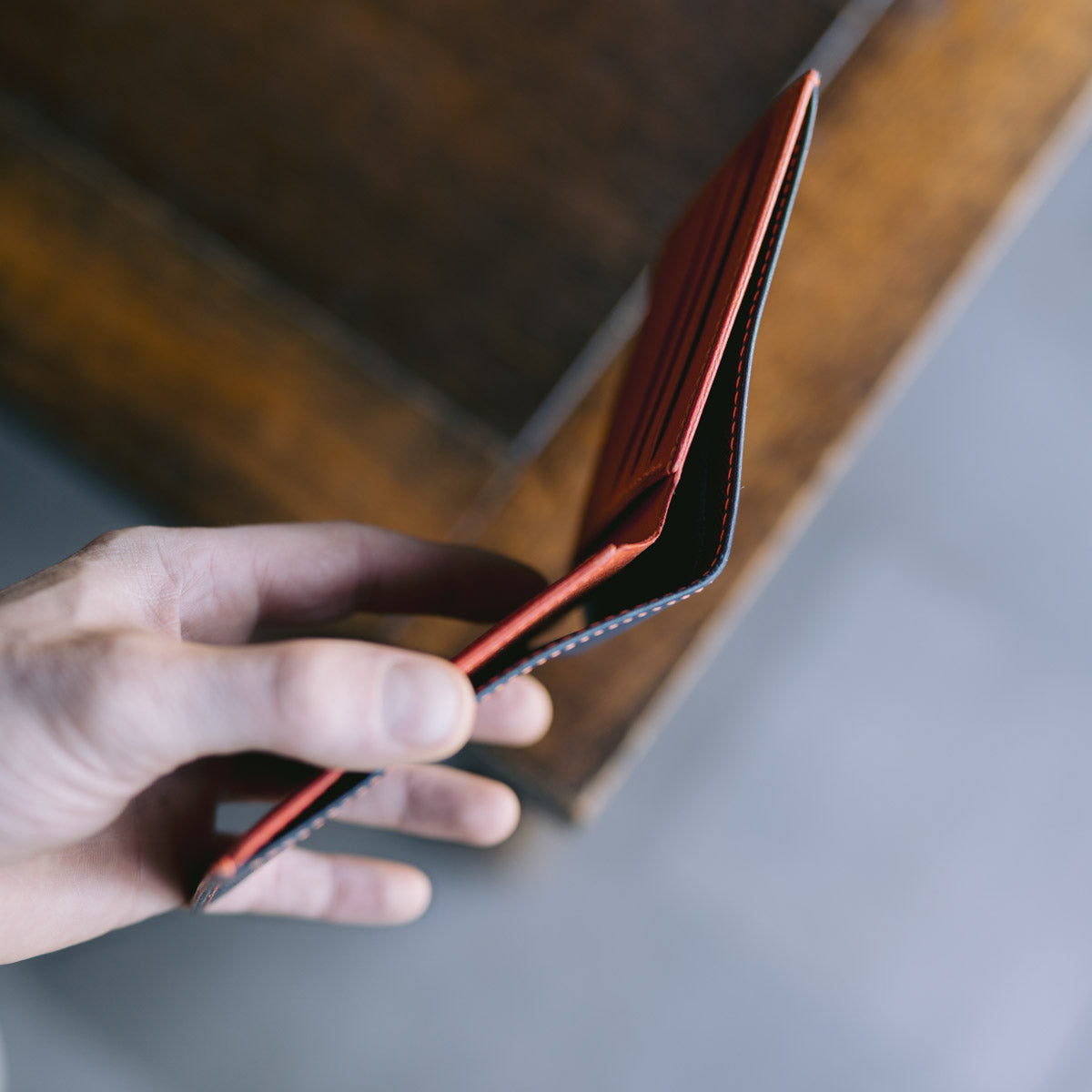 Hand holding a blue leather wallet with orange interior