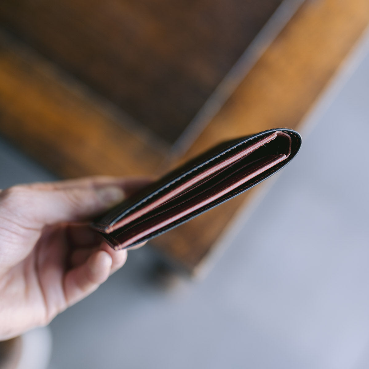 Hand holding an open black and brown leather wallet with a blurred background