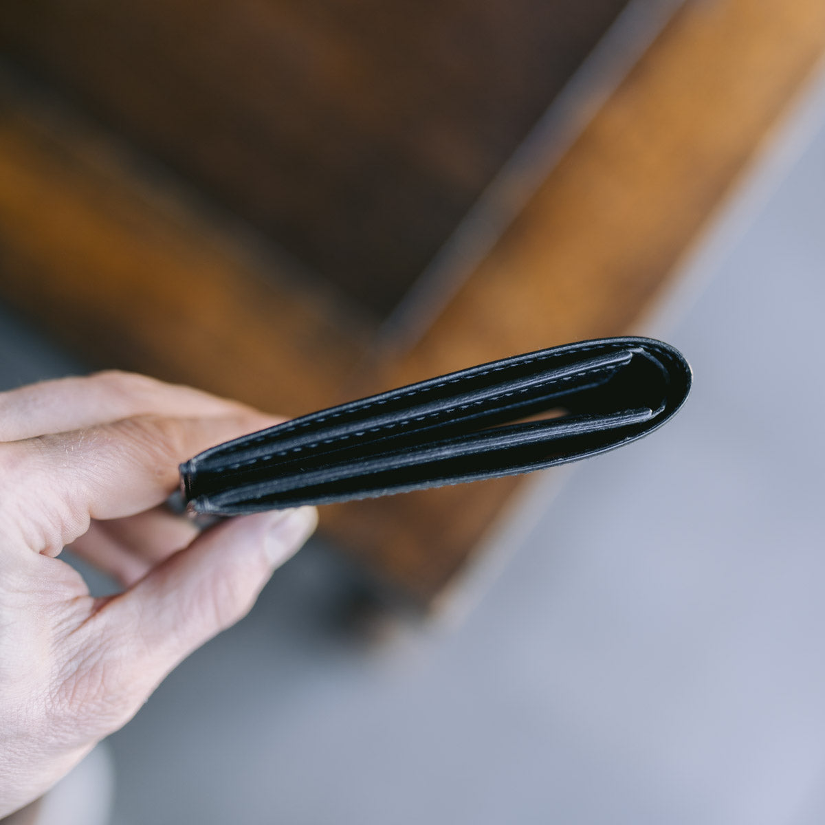 Hand holding a black leather wallet against a blurred background