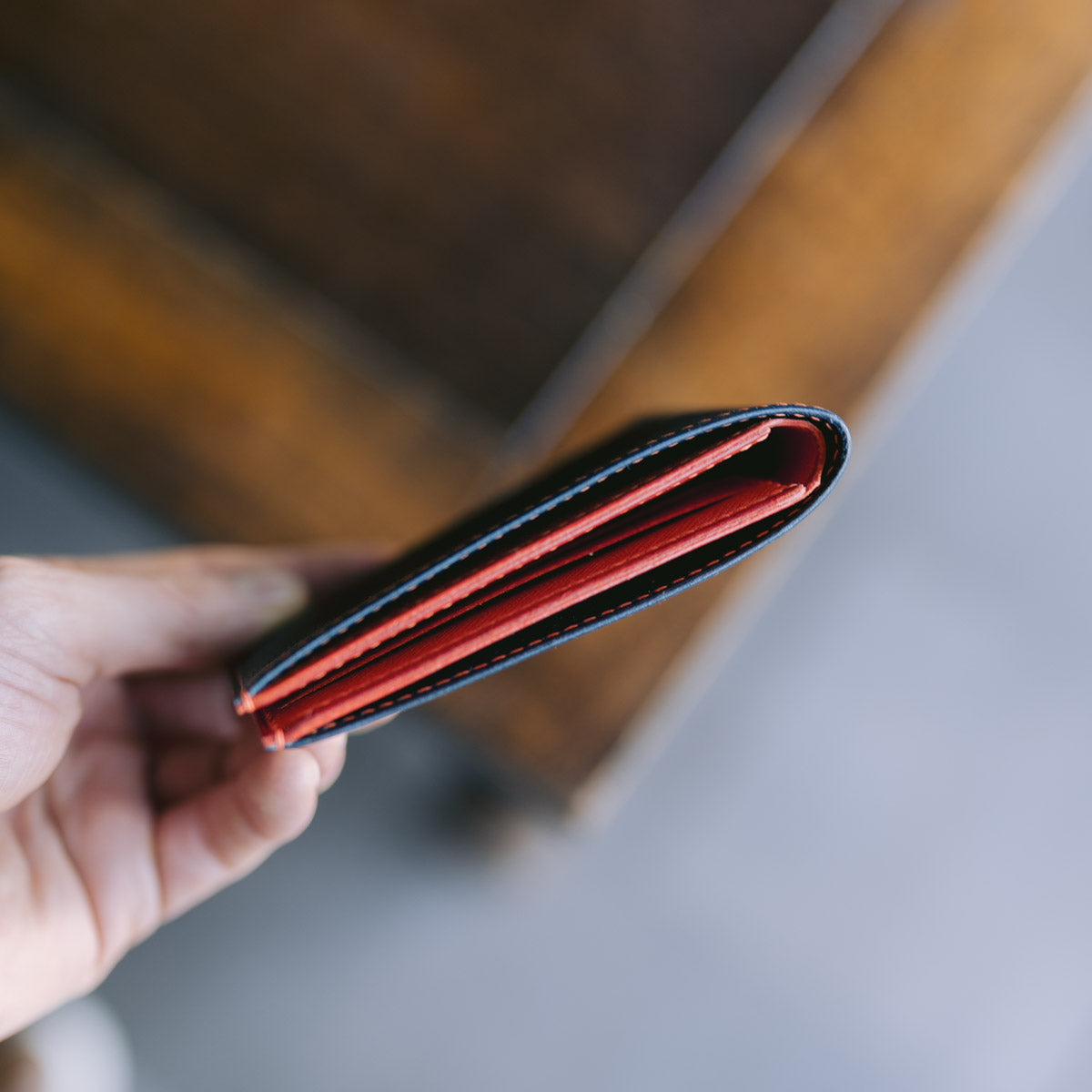 Hand holding a blue leather wallet with orange interior