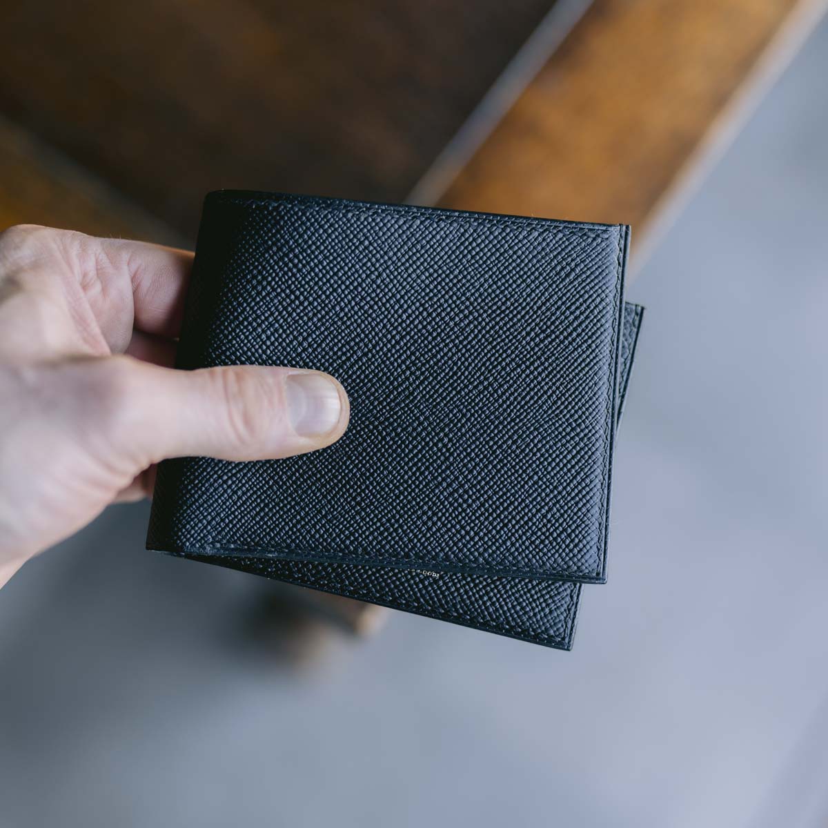Hand holding a black textured wallet against a neutral background