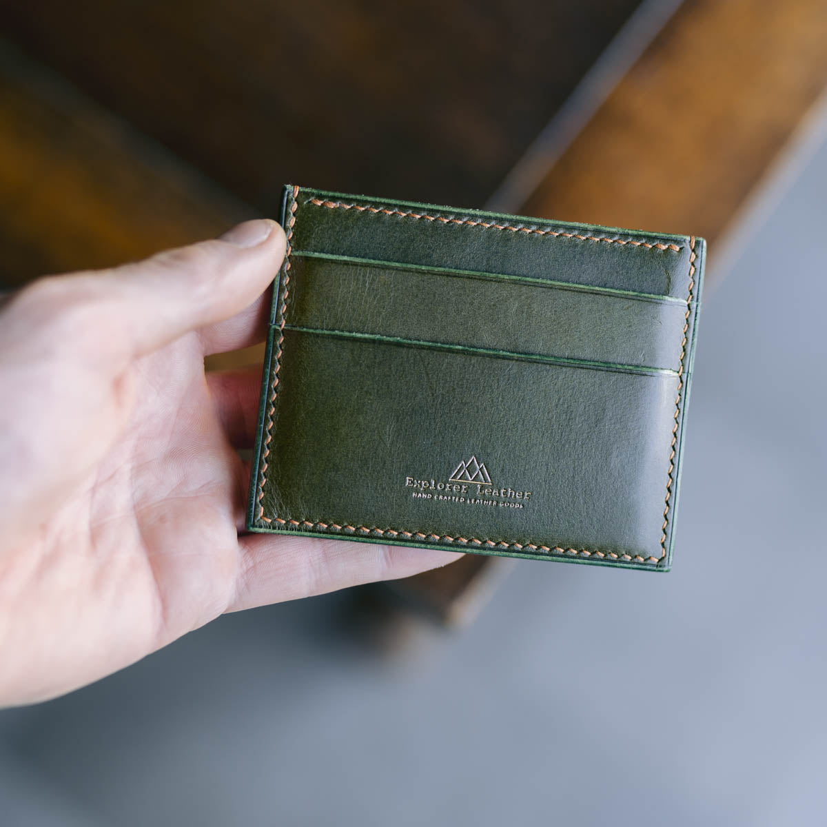 Hand holding a green leather wallet with a blurred background