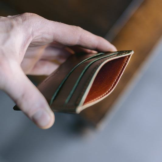 Hand holding a green leather card holder with brown leather lining with a blurred background