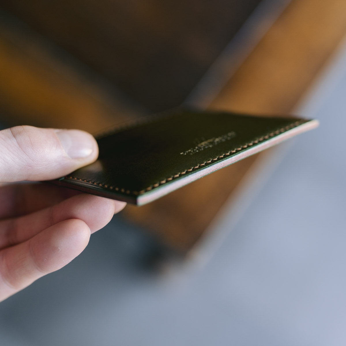 Hand holding a green leather card holder against a blurred background