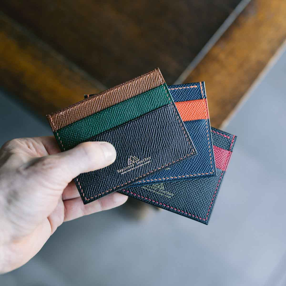 Hand holding a stack of colorful leather card holders on a neutral background