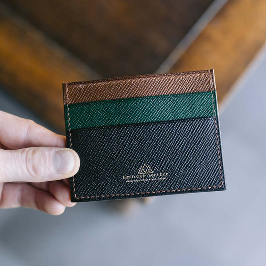 Hand holding a black, green and brown leather cardholder with a visible explorer leather brand logo.
