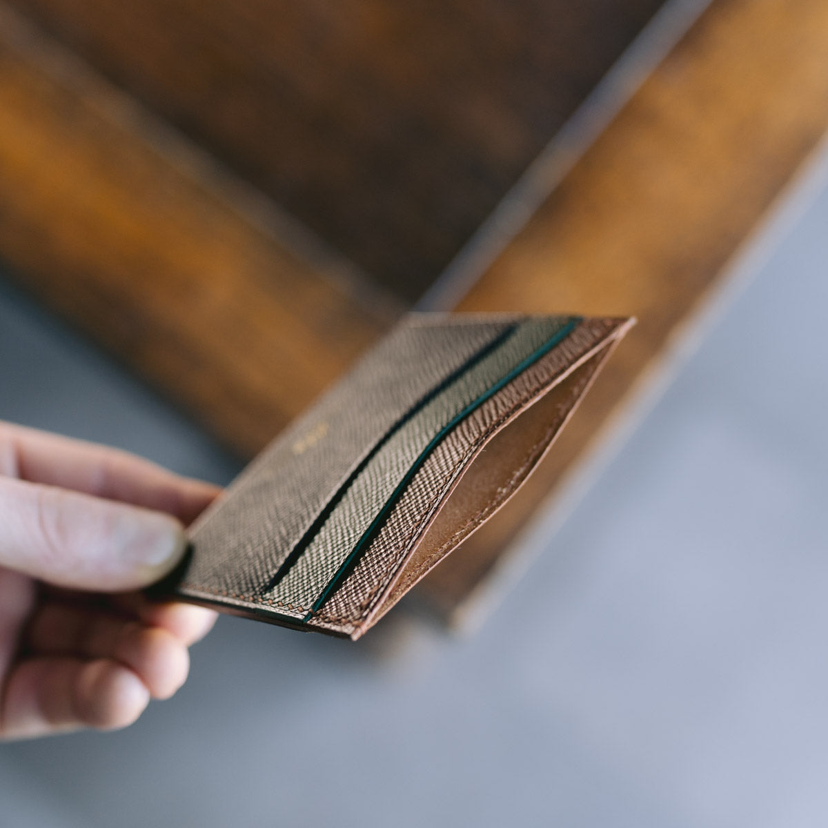 Hand holding a black, green and brown leather cardholder 