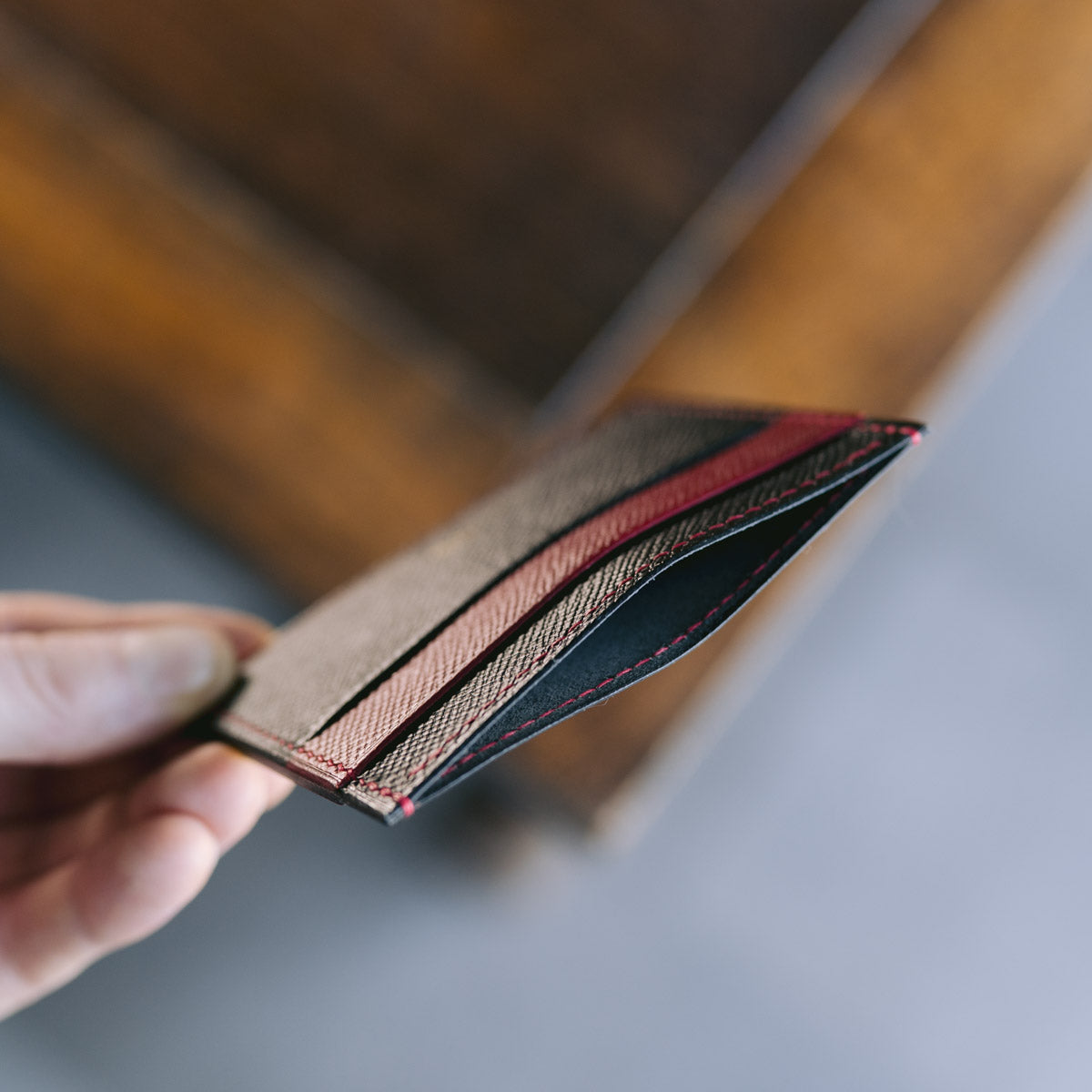 Hand holding a leather card holder in black and red with a blurred background