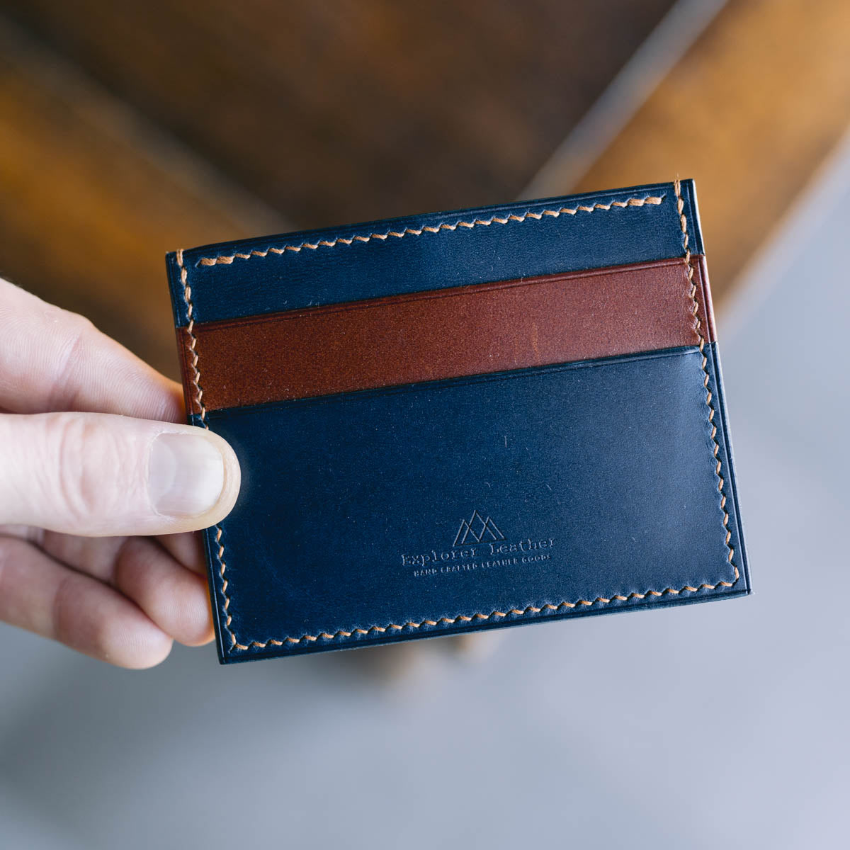 Blue and brown leather cardholder held by a hand on a blurred background