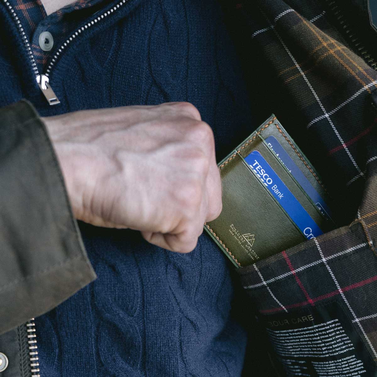 Person pulling a green card holder out of a plaid jacket pocket.