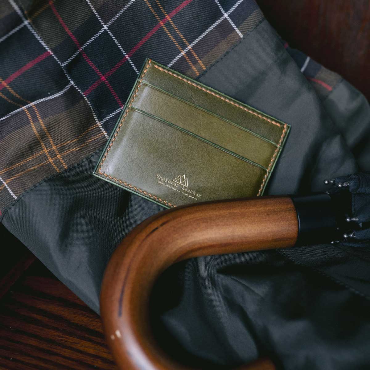 Green card holder wallet with wooden umbrella handle on plaid coat