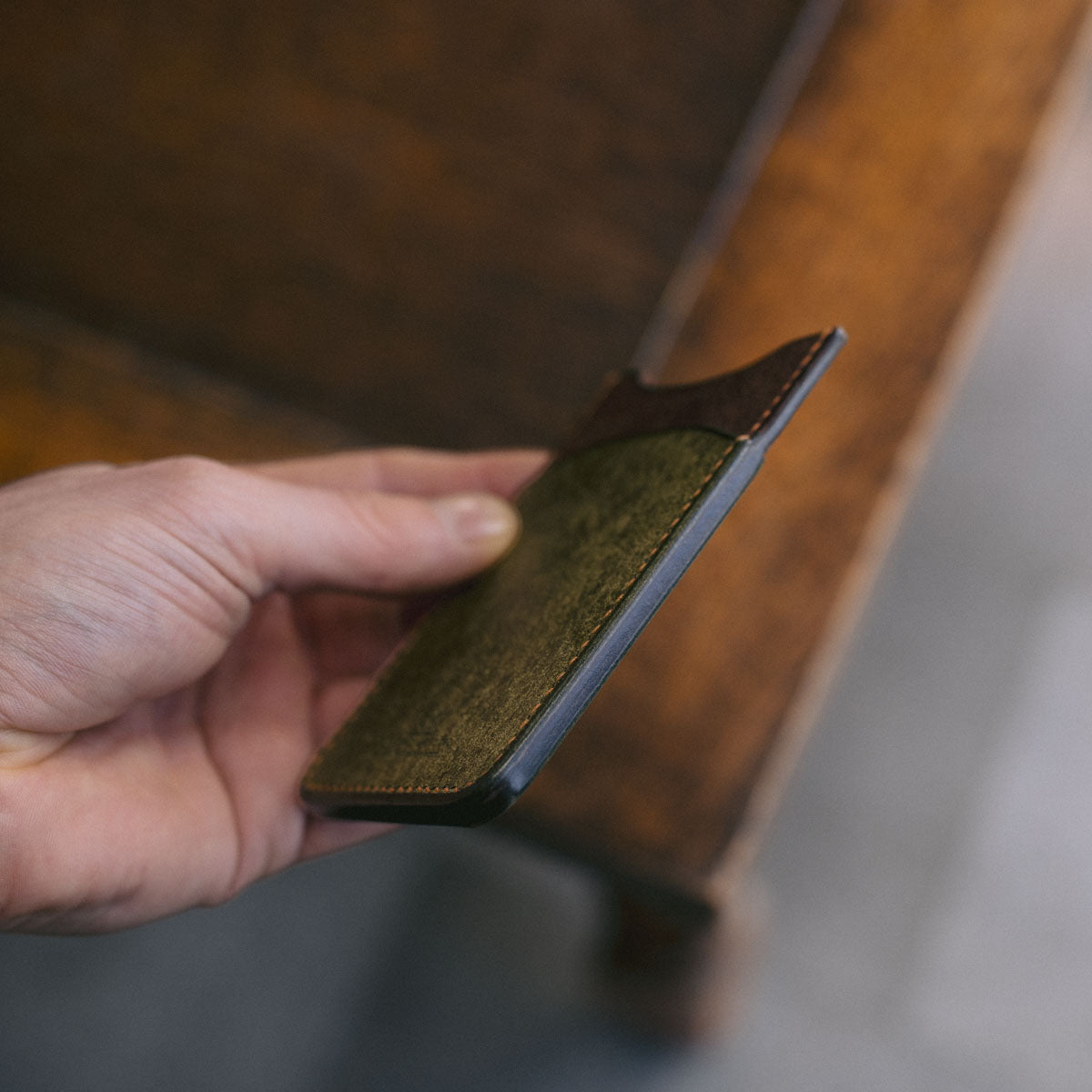 Hand holding a Green and Brown leather cardholder on a wooden surface.