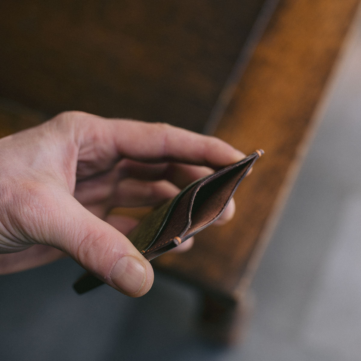 Hand holding a Green and Brown leather cardholder on a wooden surface. Showing it open