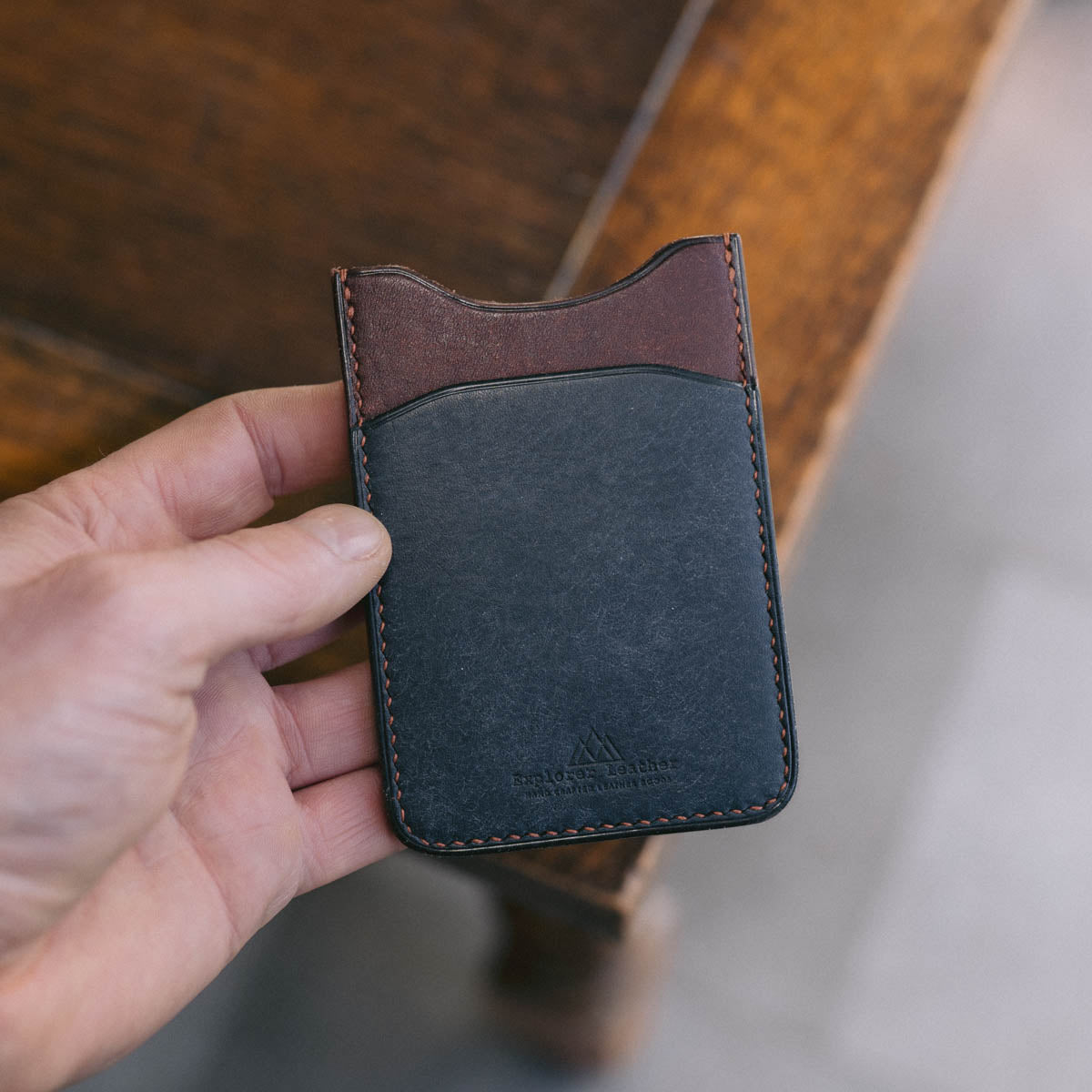Hand holding a Blue and Brown leather cardholder on a wooden surface.