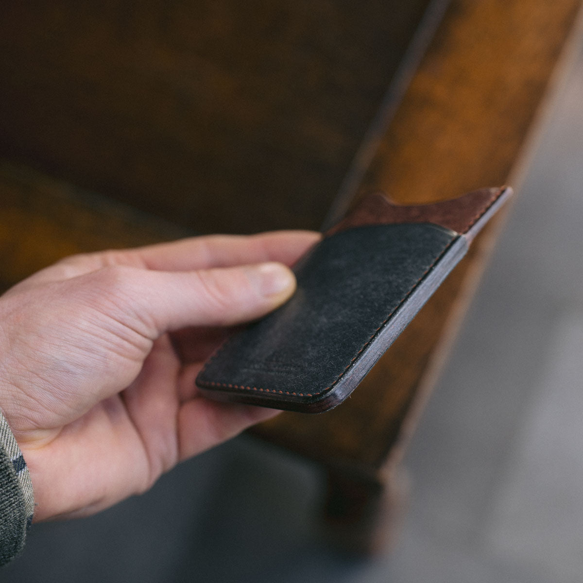 Hand holding a Blue and Brown leather cardholder on a wooden surface.