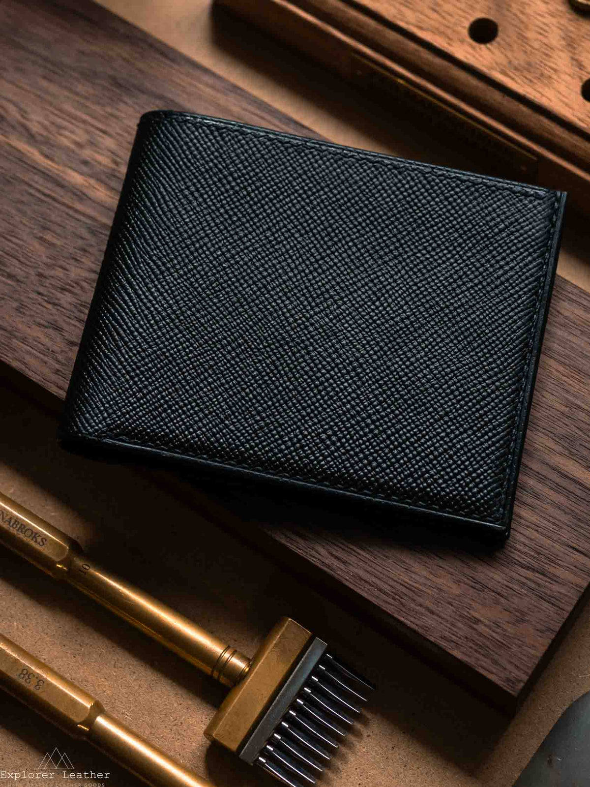 Closed black leather bifold wallet beside leatherworking tools