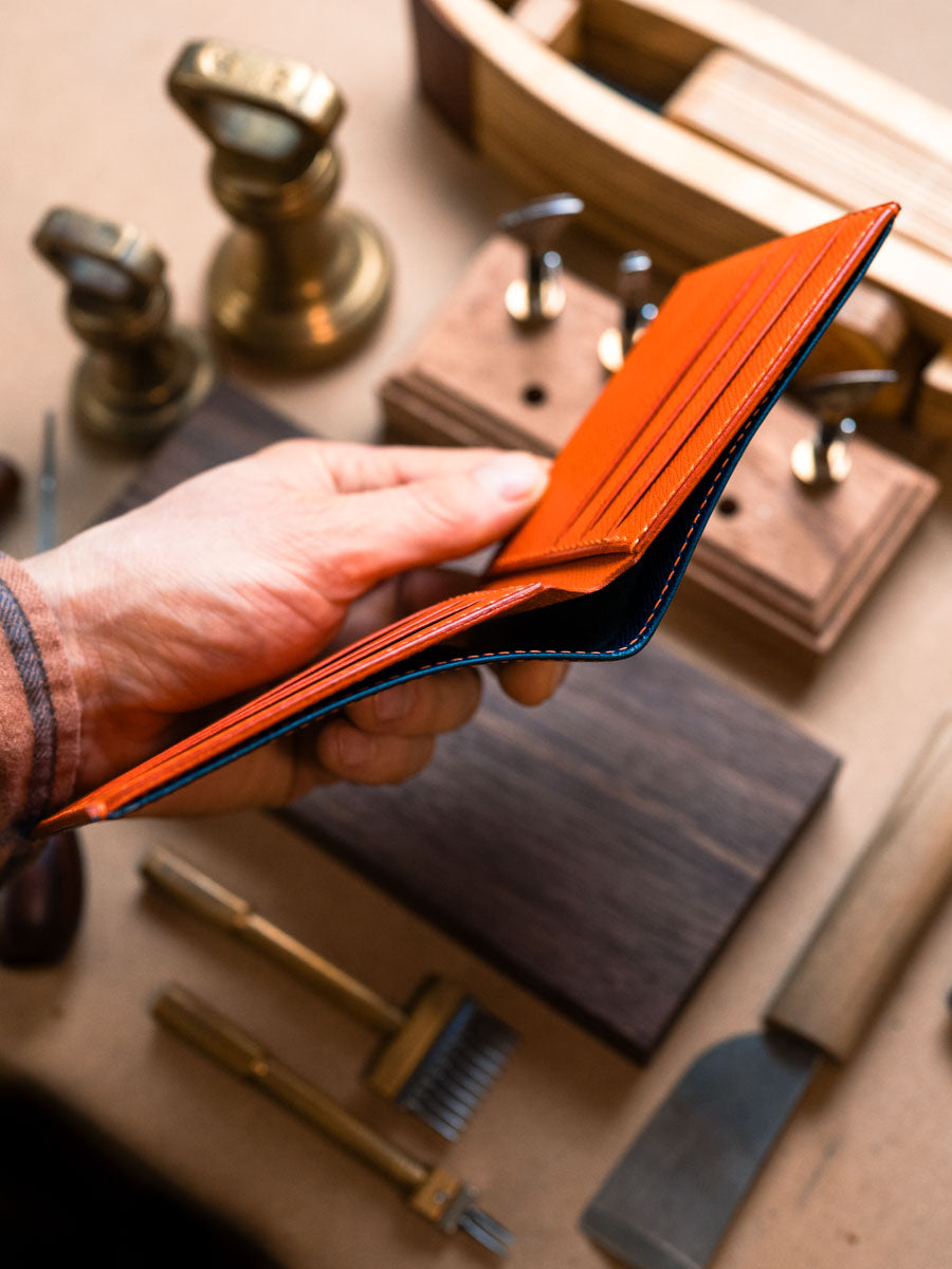 Side profile of navy leather bifold wallet with orange interior