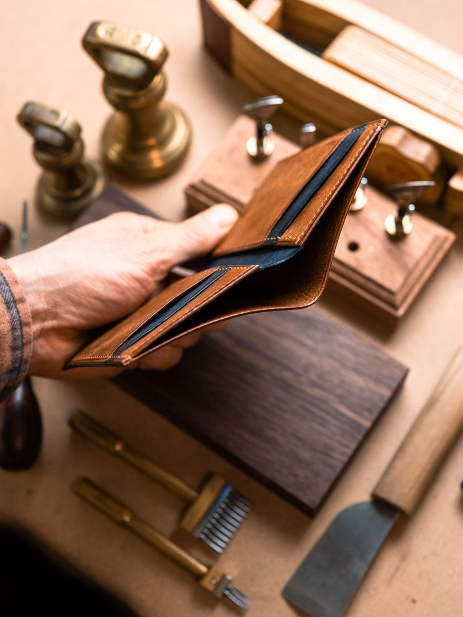 Cognac and navy vertical bifold wallet held open to show pockets